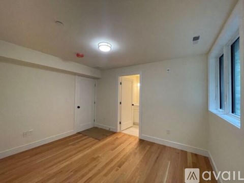A room with wooden flooring and white walls, with a doorway leading to another room.