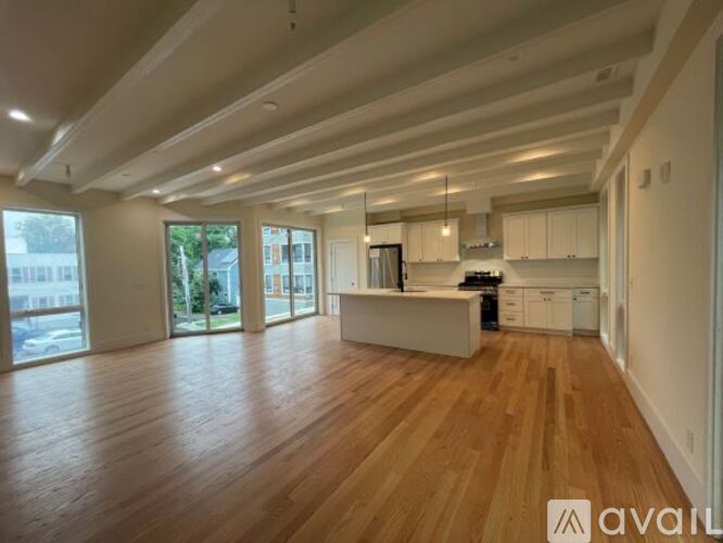 A spacious living room with wooden floors and a kitchen area in the background.