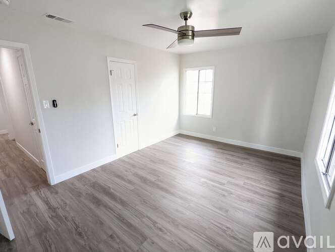 A spacious room with a ceiling fan and light, hardwood flooring, and two doors.