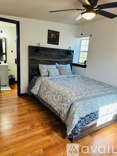 A bedroom with a bed, a ceiling fan, and a painting on the wall.