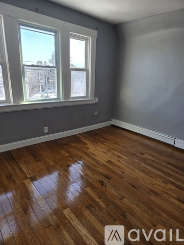 A room with wooden flooring and two windows.