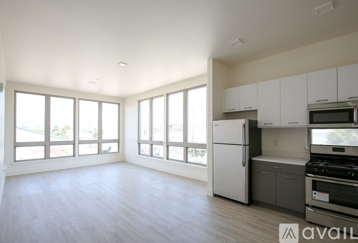 A spacious kitchen with white cabinets and appliances, large windows, and a wooden floor.