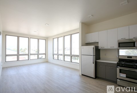 A spacious kitchen with white cabinets and appliances, large windows, and a wooden floor.