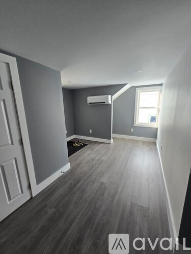 A room with grey walls and wooden flooring with a window.