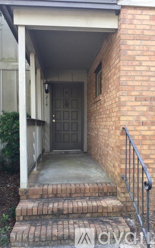 A front porch with a black door and a brick wall.