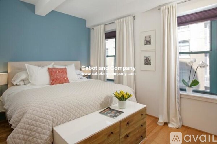 A bedroom with a white bed and a white nightstand with a vase of flowers on top.