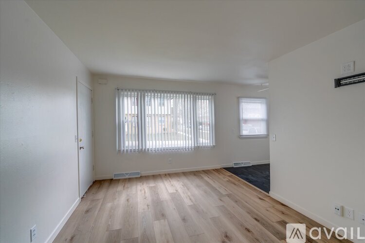 A room with wooden floors and white walls, with a window covered by white blinds.
