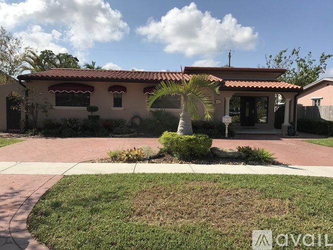 A house with a red roof and a palm tree in front.