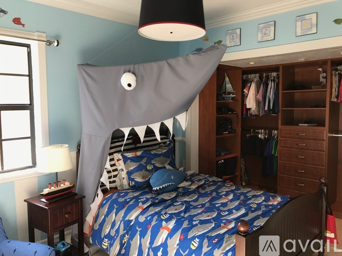 A bedroom with a bed covered in a blue and white shark print comforter.
