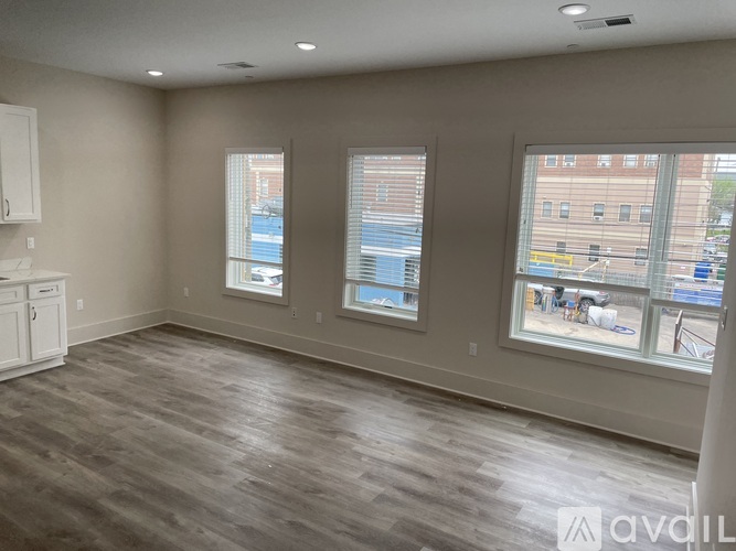 A spacious room with wooden flooring and two windows showing an outdoor view.