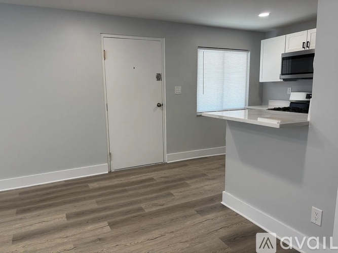 A spacious room with a ceiling fan and lighting, featuring a kitchen area with white cabinets and a countertop.