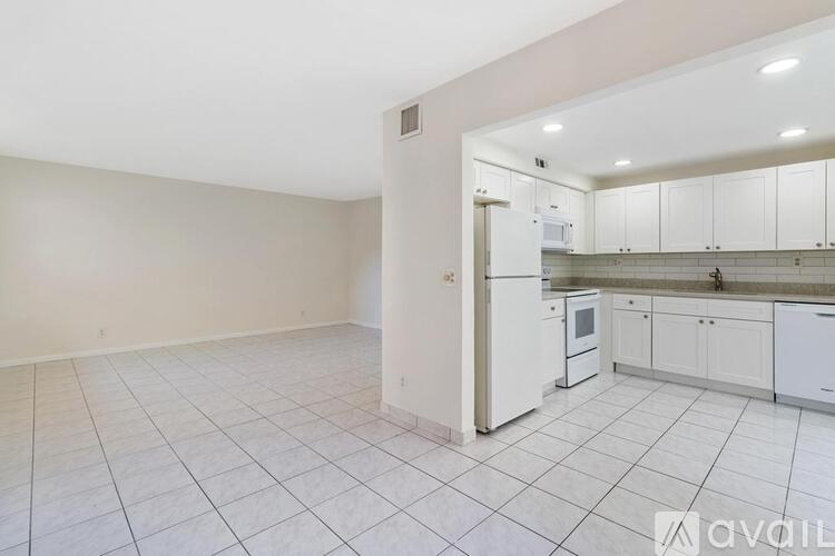 A kitchen with white cabinets and appliances in a room with white tiled flooring.