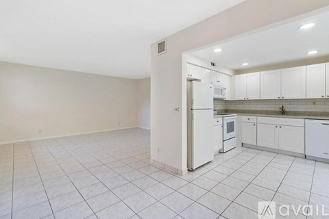 A kitchen with white cabinets and appliances in a room with white tiled flooring.