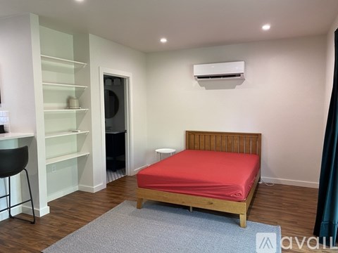 A bedroom with a red bed and a white wall.