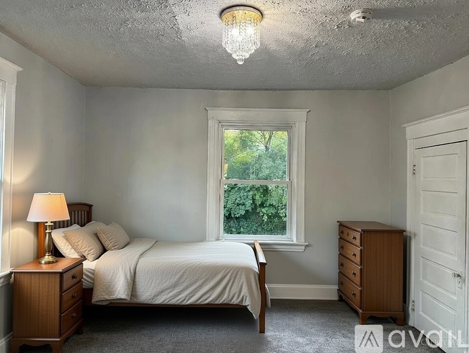 A bedroom with a bed, nightstand, and window.