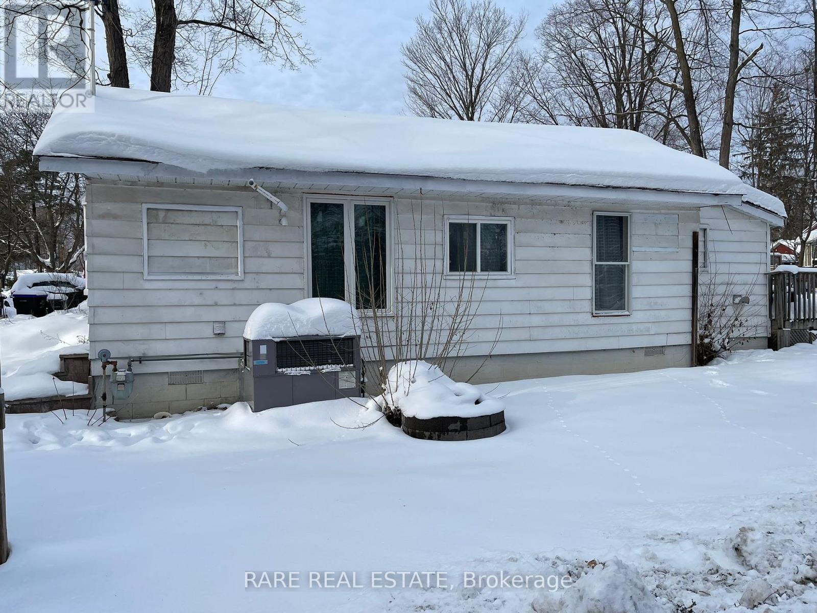 A small house with a snow-covered roof and a small tree in front of it.