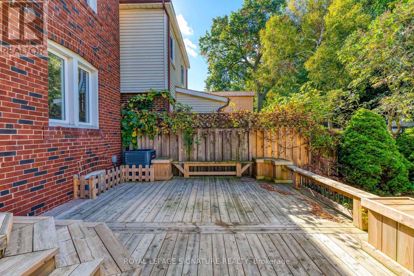 A wooden deck with a bench and a table surrounded by a brick wall and trees.