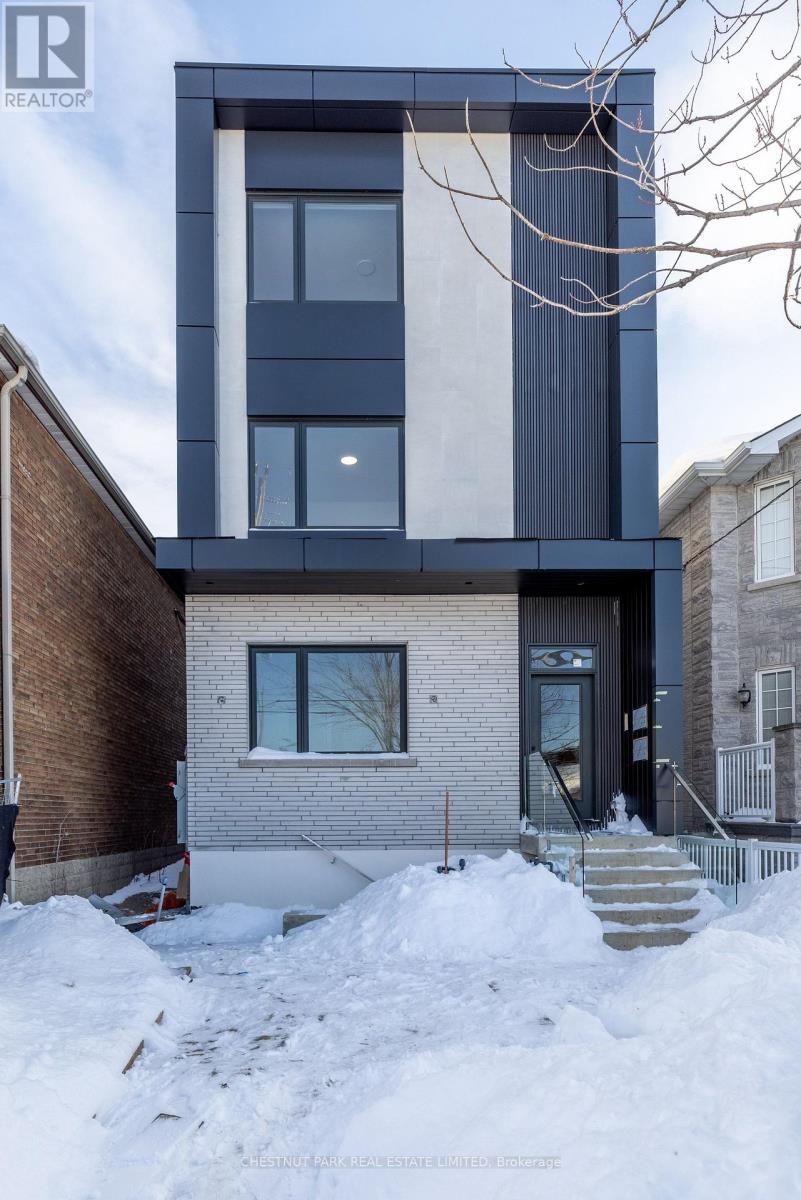 A modern house with a black and white facade stands in front of a snow bank.