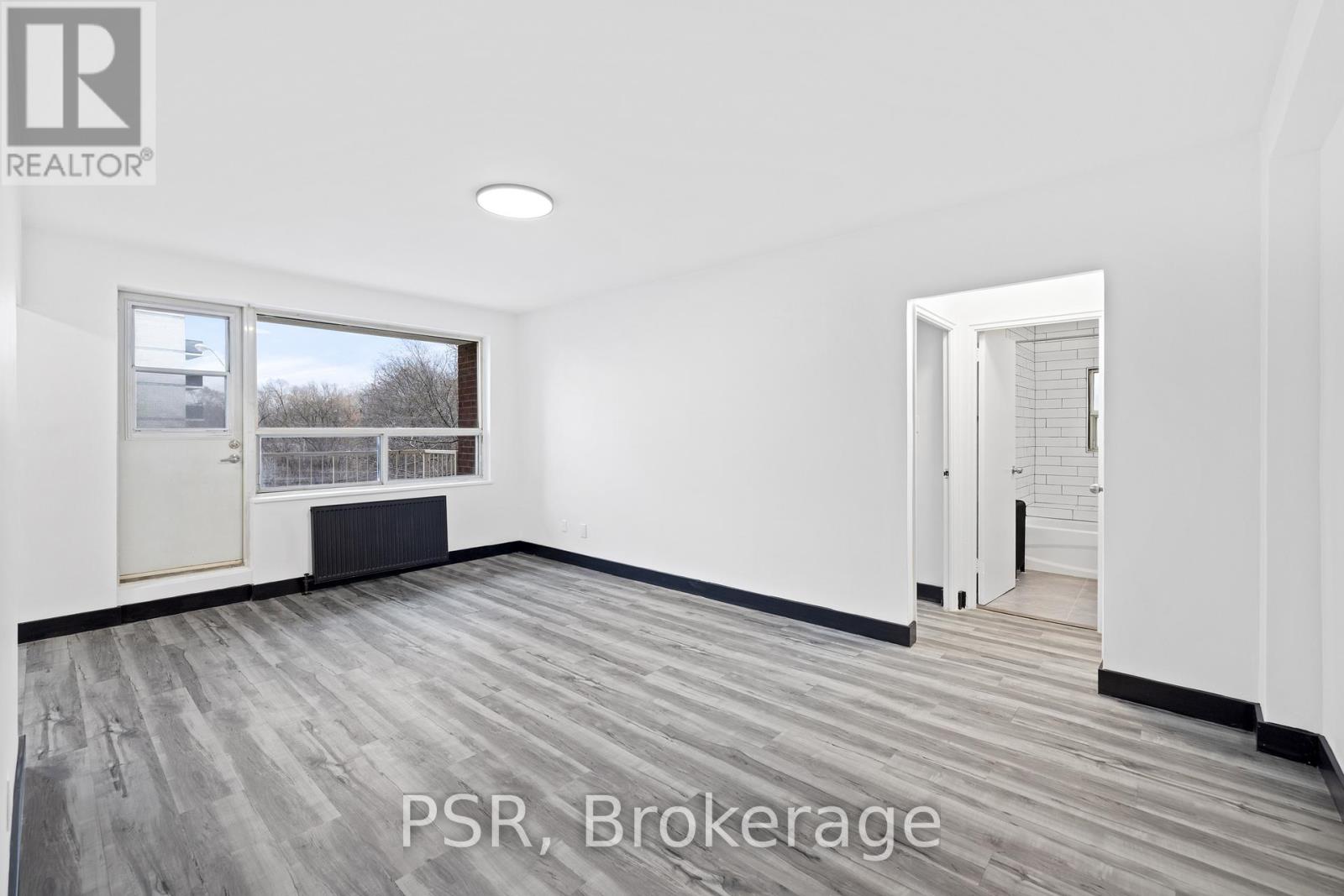 A room with a large window and a door leading to another room.