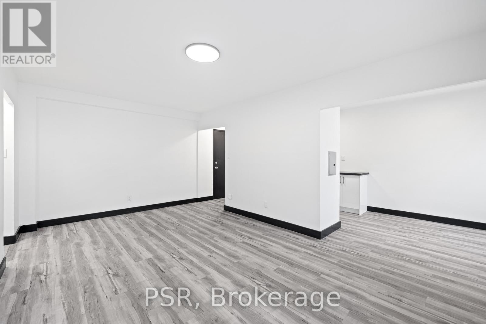 A room with a wooden floor and white walls, with a door on the left and a small table on the right.