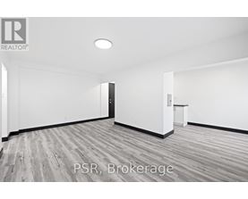A room with a wooden floor and white walls, with a door on the left and a small table on the right.