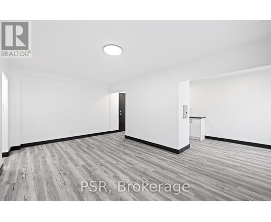 A room with a wooden floor and white walls, with a door on the left and a small table on the right.