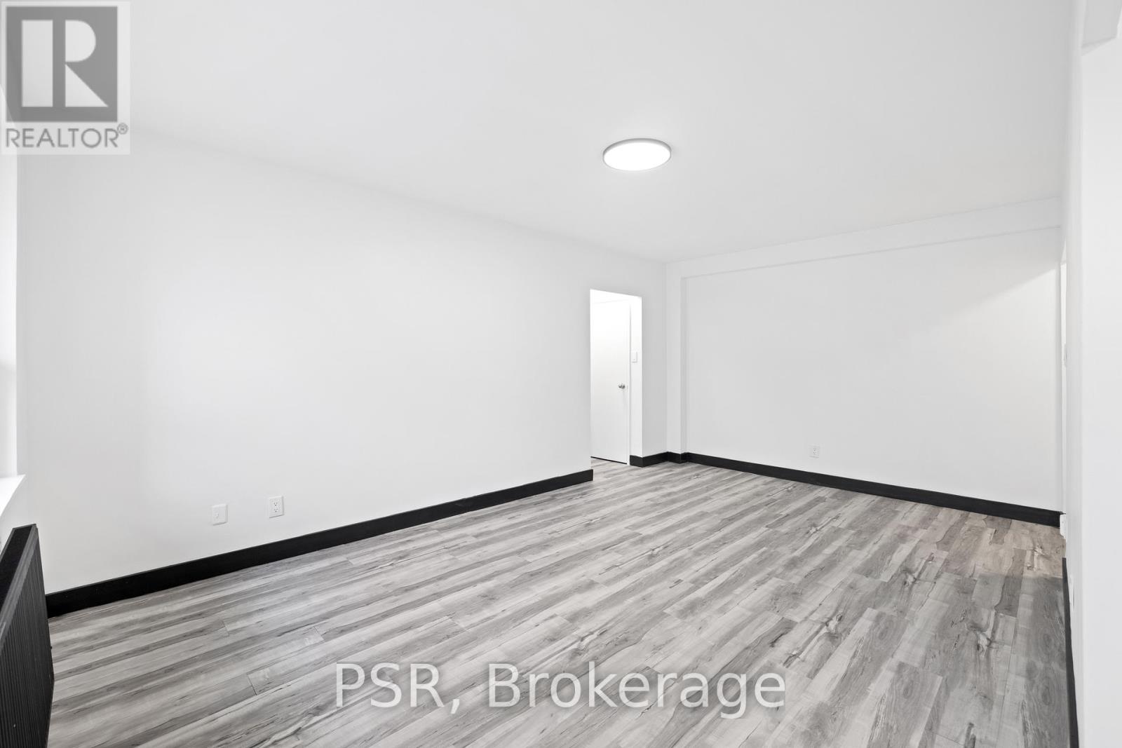 A room with a wooden floor and white walls, with a door in the background.