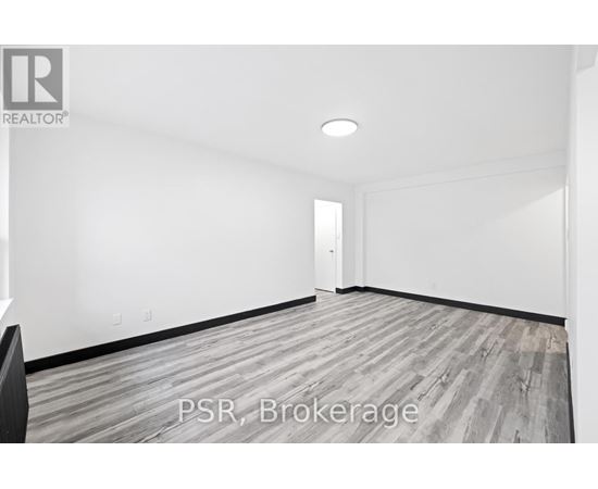 A room with a wooden floor and white walls, with a door in the background.