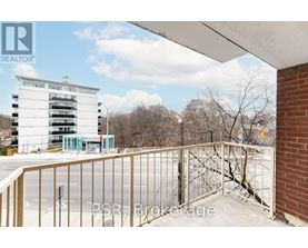 A balcony with a metal railing overlooks a parking lot and a multi-story building.