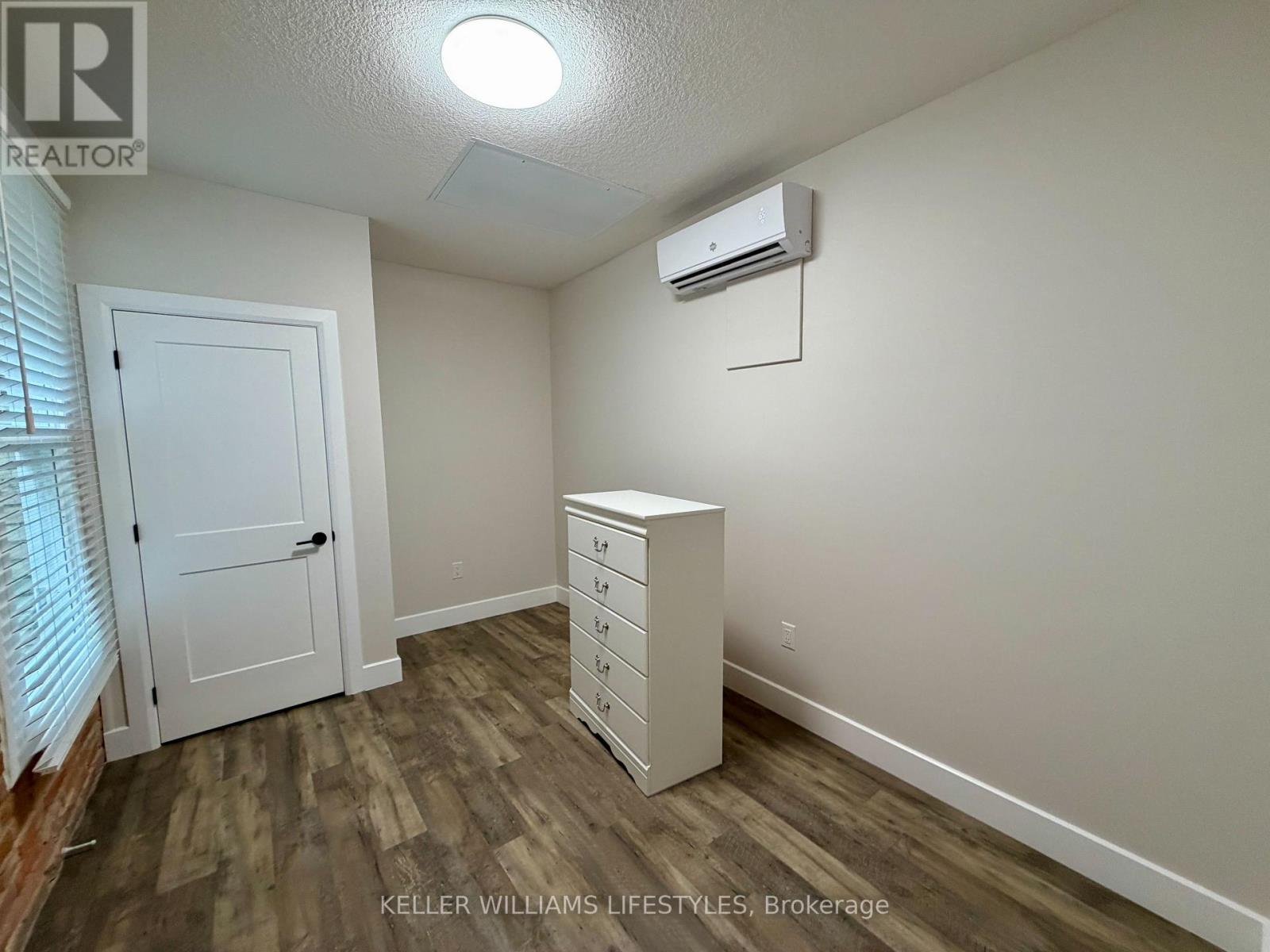 A bedroom with a white dresser and a window with blinds.