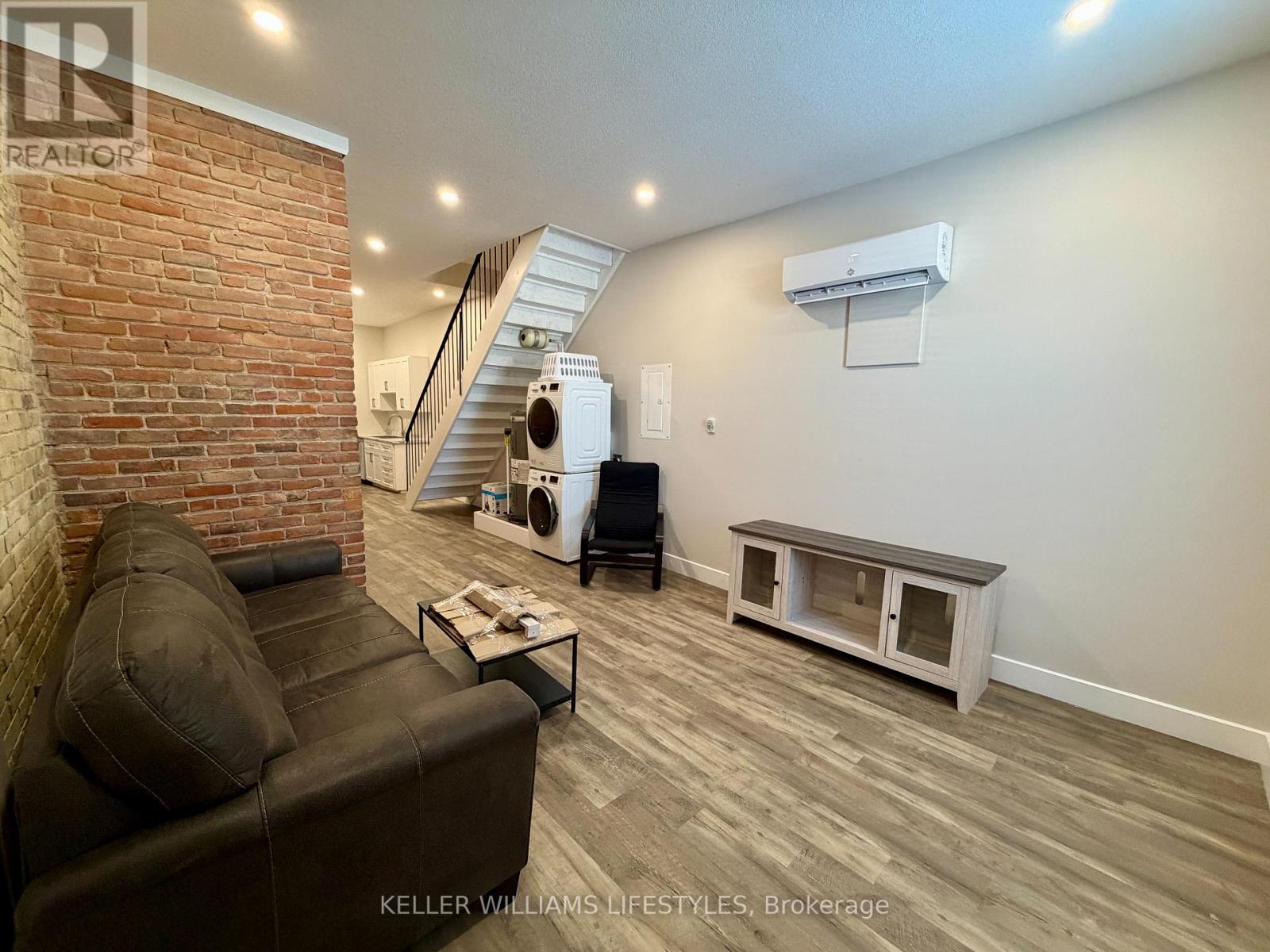 A living room with a brown leather couch and a brick wall.