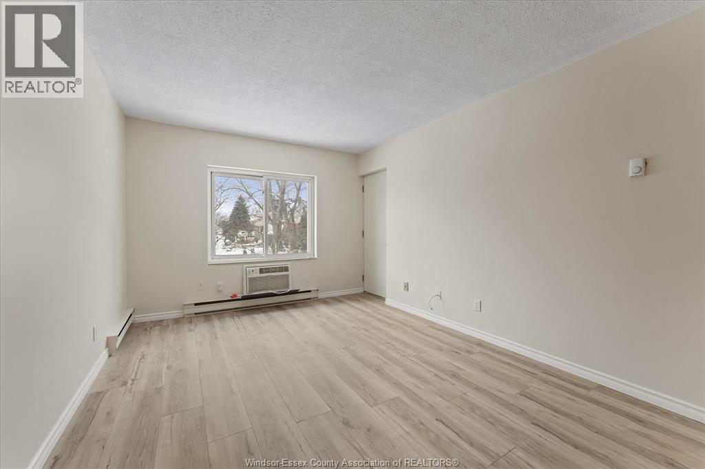 A spacious room with wood flooring and a window showing a tree outside.
