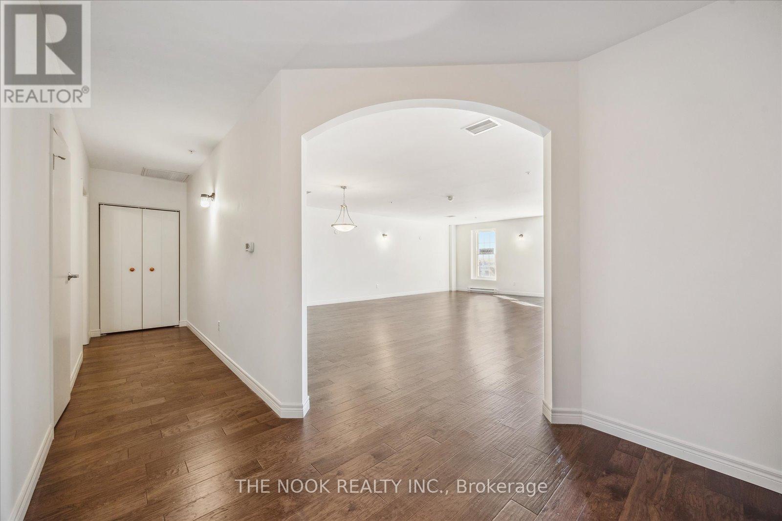 A spacious room with wooden floors and white walls, with a door on the left and a window on the right.