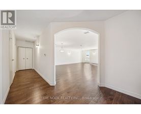 A spacious room with wooden floors and white walls, with a door on the left and a window on the right.