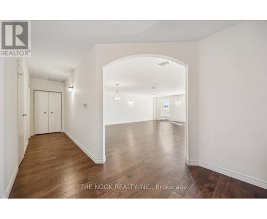A spacious room with wooden floors and white walls, with a door on the left and a window on the right.