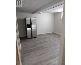 A room with a fridge and wood flooring.