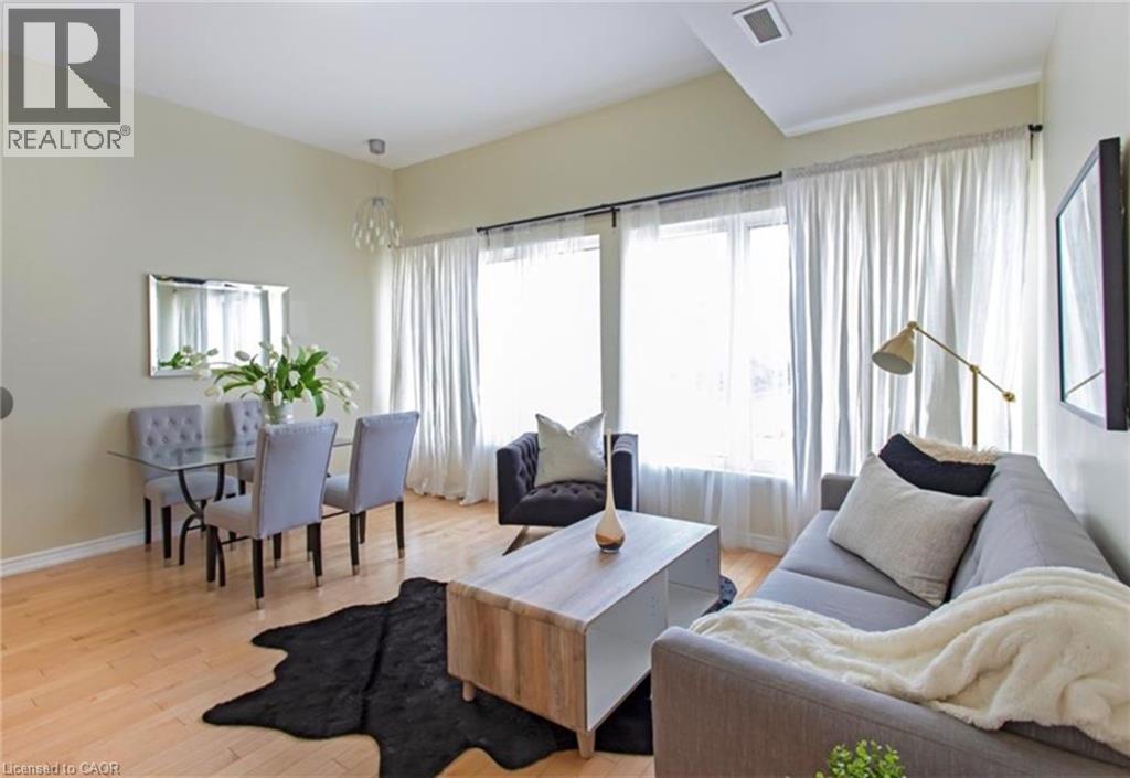 A living room with a grey couch, a coffee table, a dining table with chairs, and a large window with curtains.