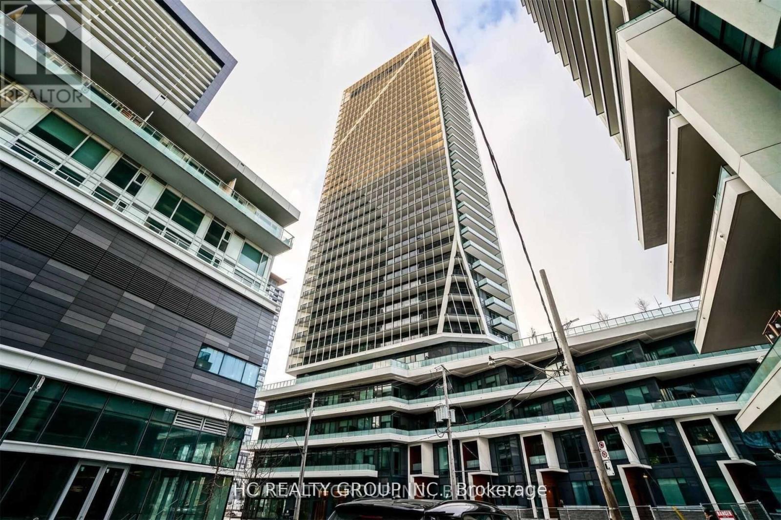A tall building with a glass facade stands in front of a cluster of smaller buildings.