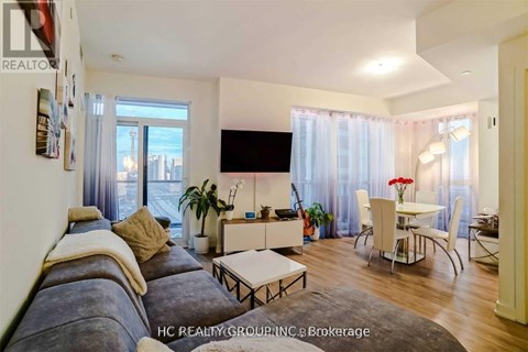 A living room with a grey couch, a white coffee table, a flat screen TV, and a dining table with chairs.