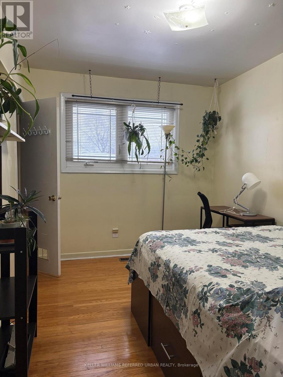 A bedroom with a bed, desk, chair, and plants.