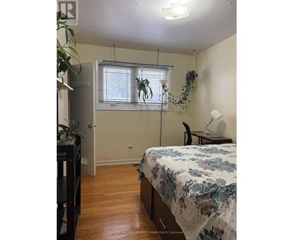 A bedroom with a bed, desk, chair, and plants.