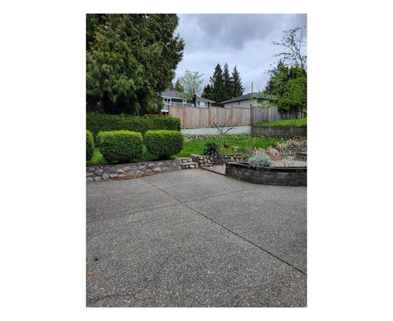 A concrete patio with a small garden in front of a house.