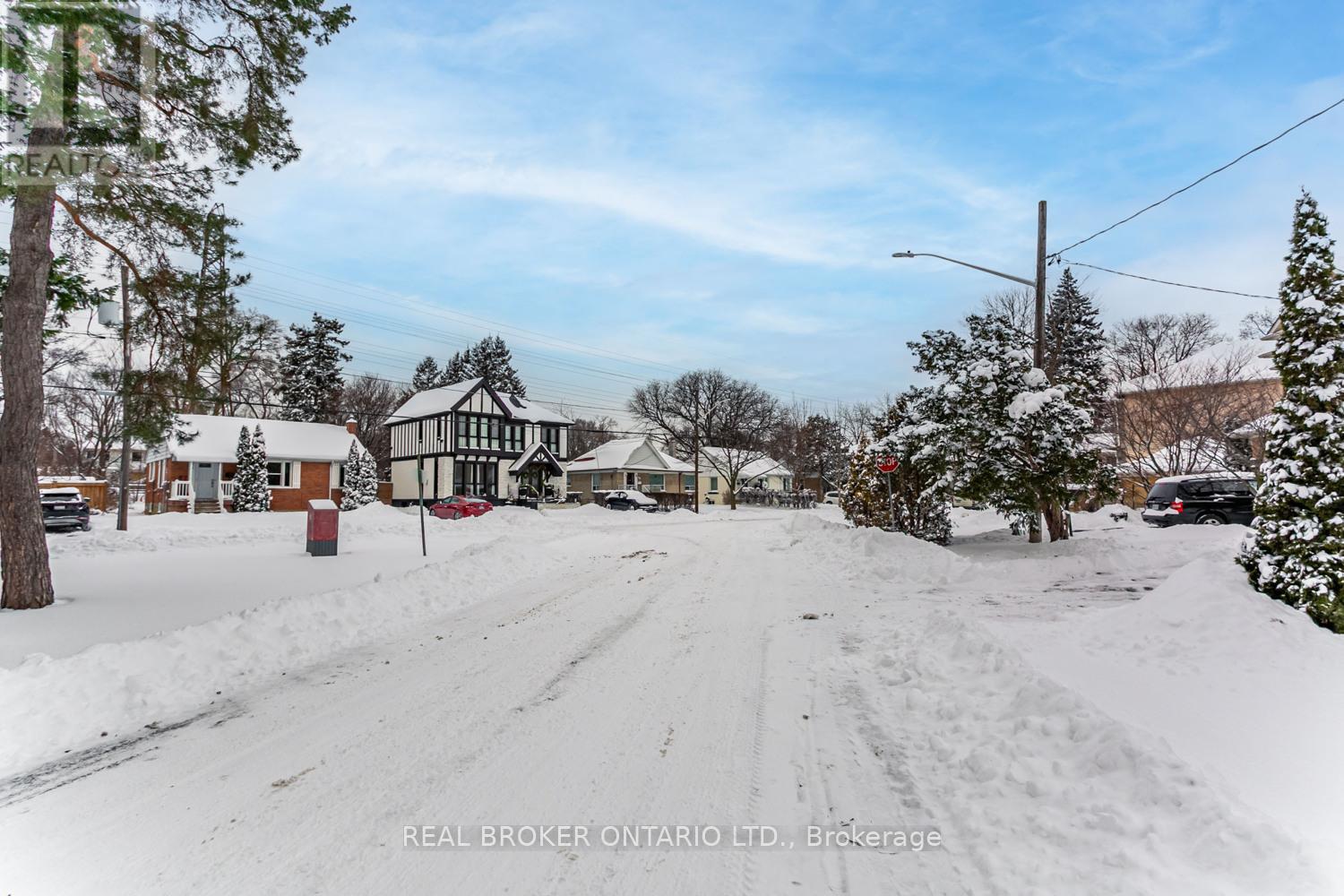 A snowy street with a house and trees on the side.