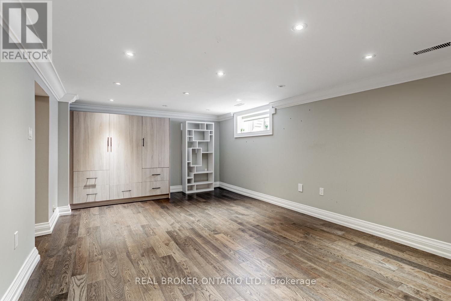 A spacious room with wood flooring and a built-in shelving unit.