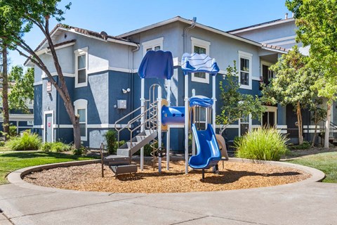 A playground with a blue slide and a play structure in front of a blue and white building.