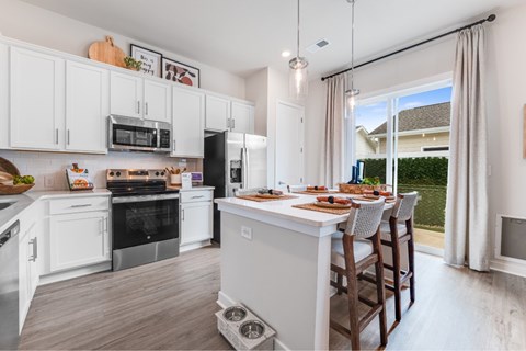 A kitchen with white cabinets and a large island with chairs around it.