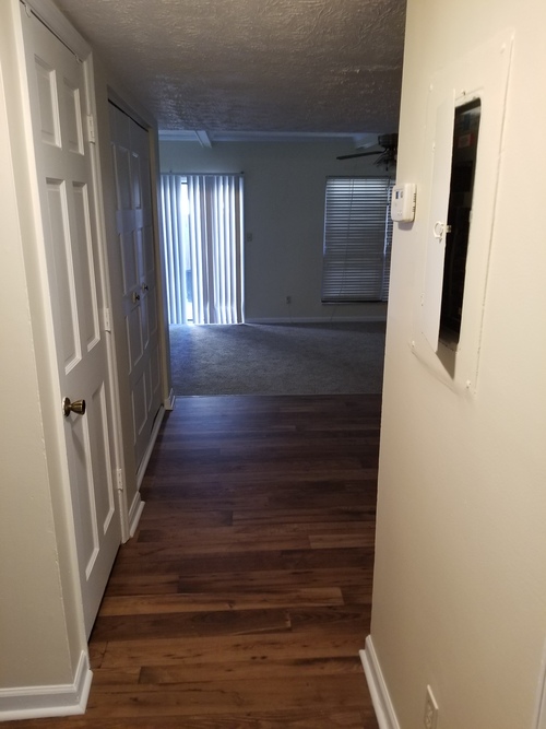 A long hallway with a door on the left and a window with blinds on the right.