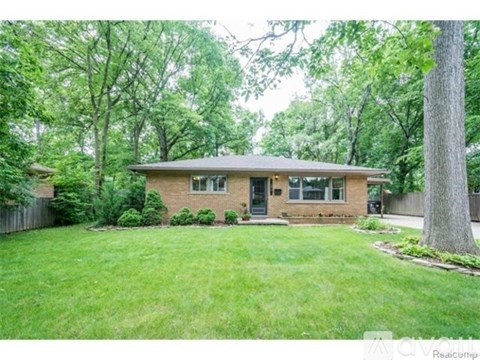 A house with a green lawn and trees in the background.