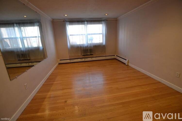 A room with wooden flooring and two windows.