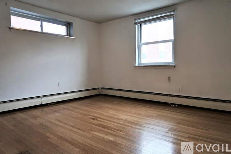 A room with wooden flooring and two windows.